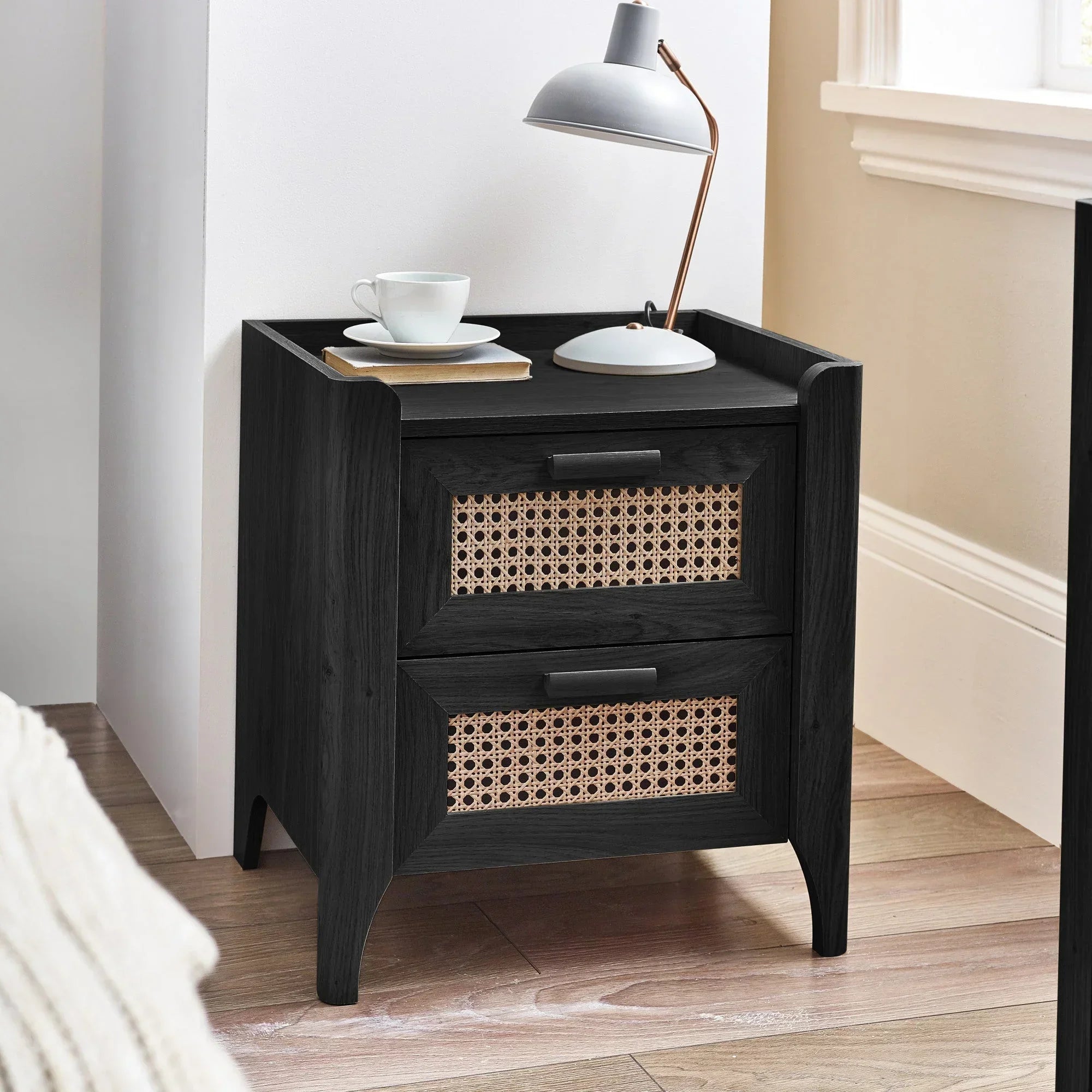 Black ash rattan effect two drawer bedside table with lamp and cup in bedroom corner