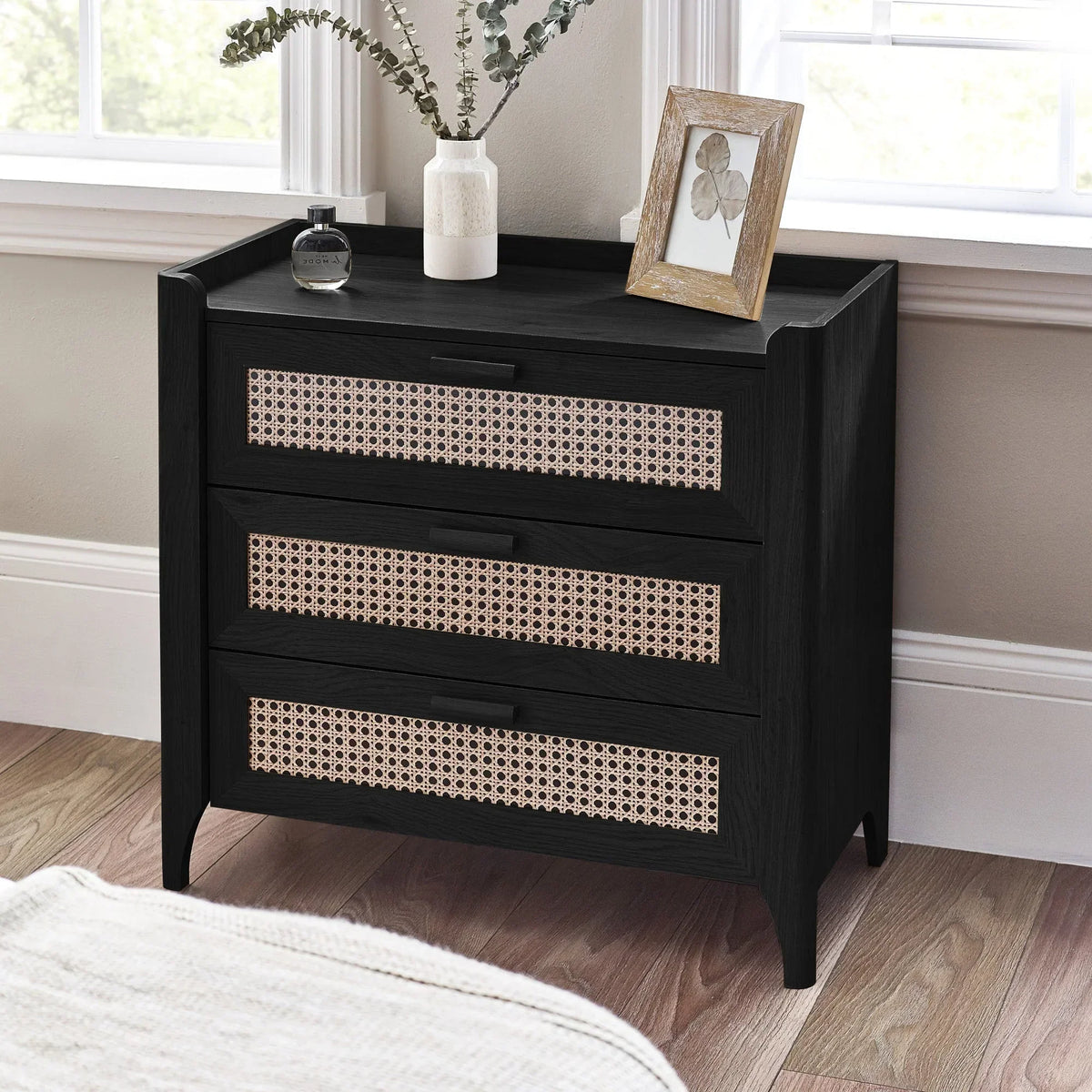 Black rattan effect 3 drawer chest in modern bedroom with wood floor and window light