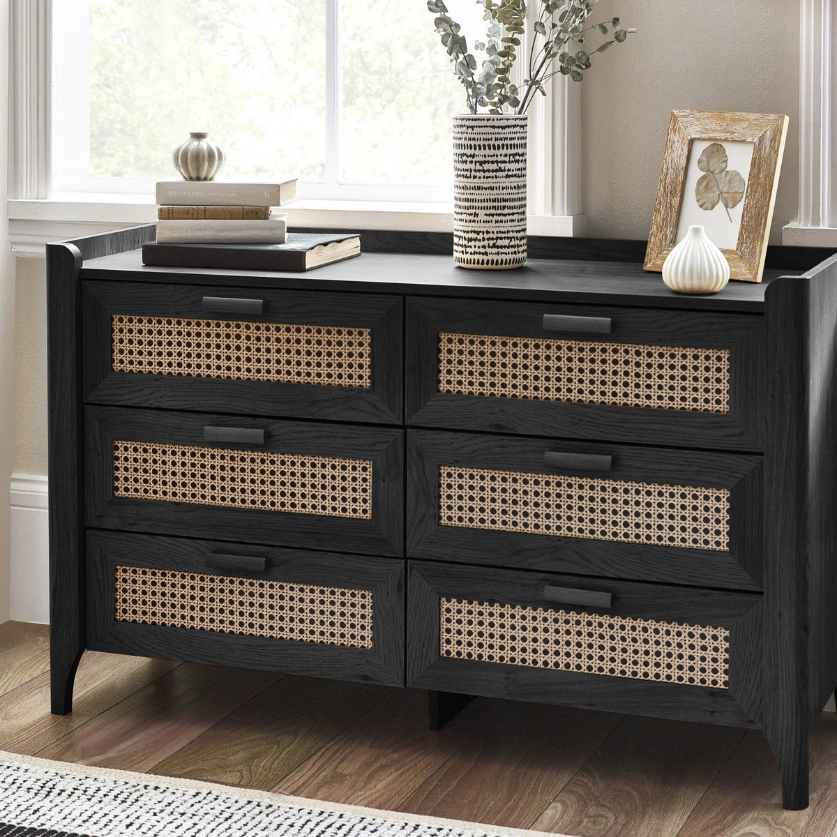 Black ash rattan effect six drawer chest below window with decor and books on top