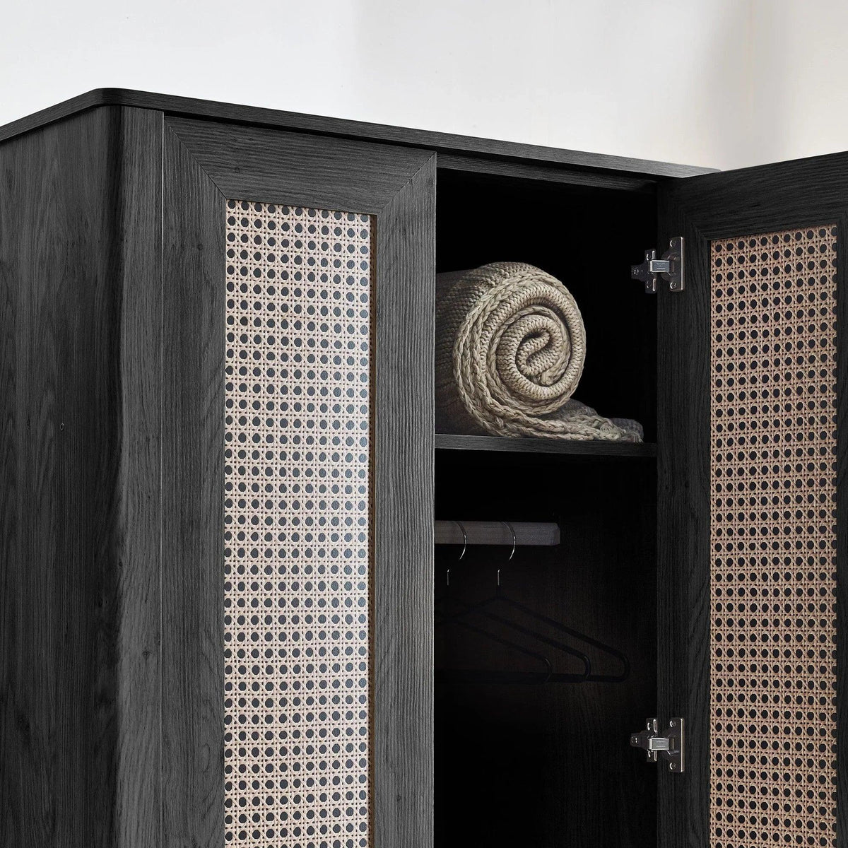 Open black ash rattan effect wardrobe with shelf, hanging rail, and rolled throw inside
