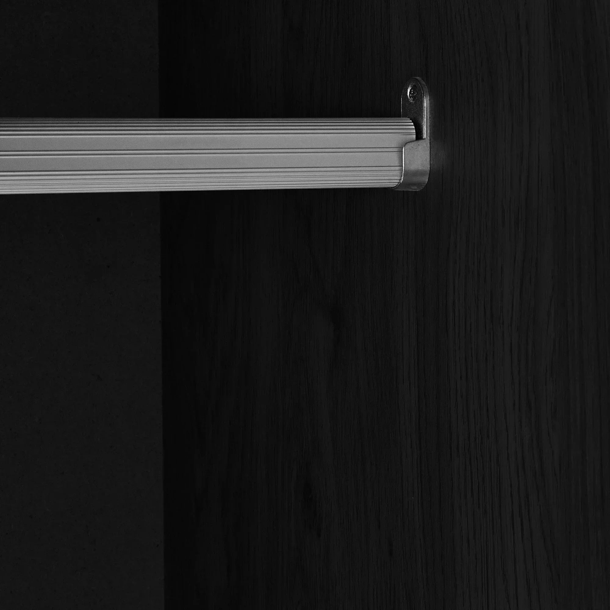 Close-up of wardrobe interior with metal hanging rail and black ash wood finish