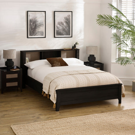 Black double bed with rattan inset storage shelves in headboard, cream bedding and brown cushion in bright bedroom