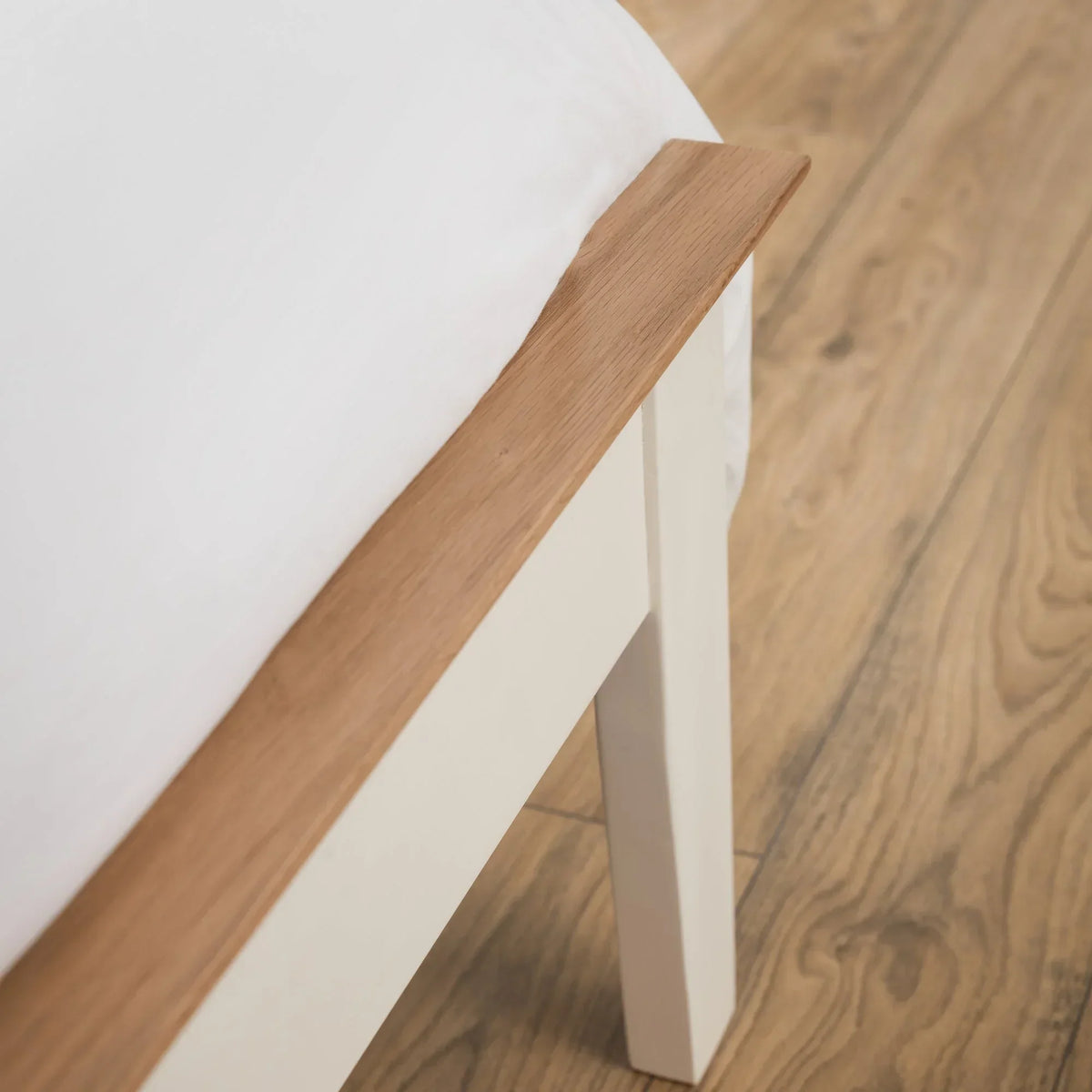 Close-up of two-tone bed frame with oak top rail and cream painted leg on wood floor