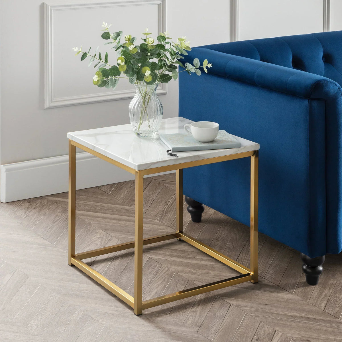 Gold frame marble side table beside blue sofa with vase and cup in living room setting