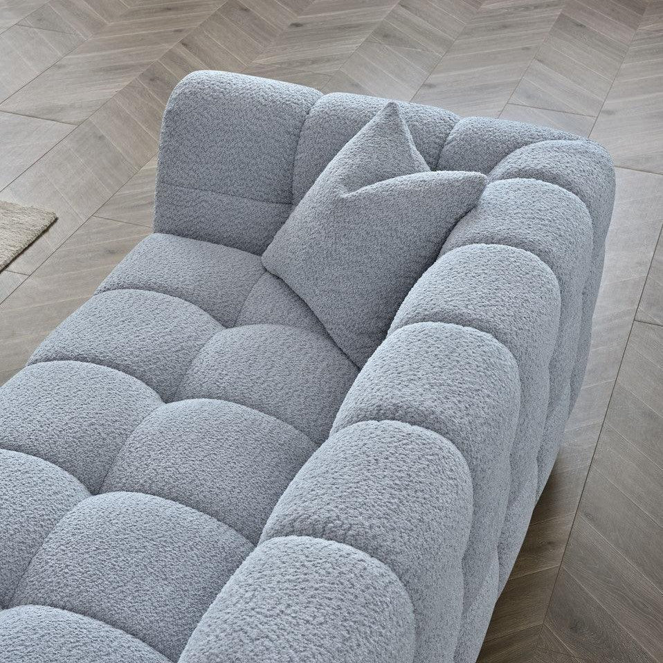 Light grey textured fabric sofa with matching cushion on herringbone wood floor
