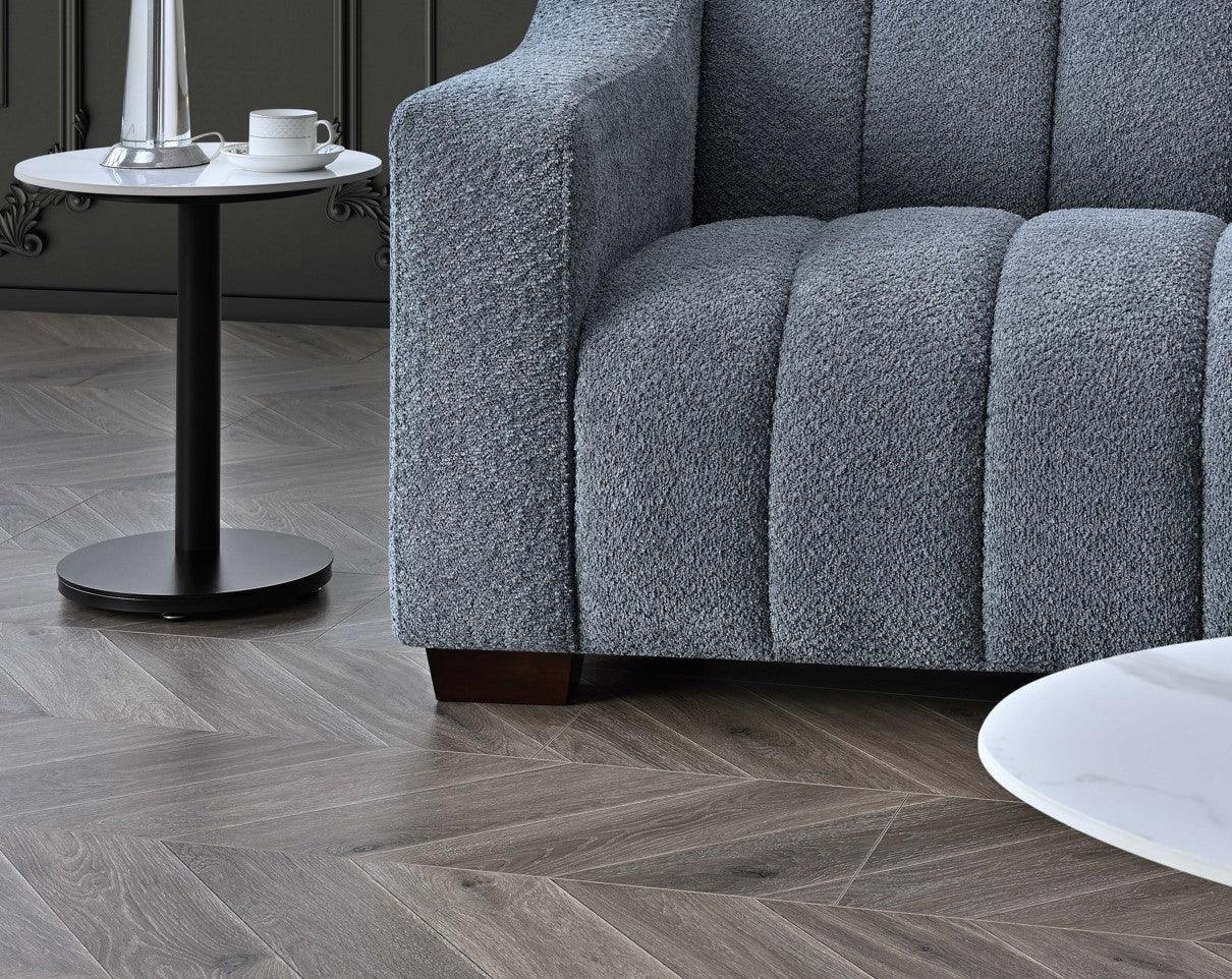 Textured grey fabric sofa with channel tufting beside round side table on herringbone floor