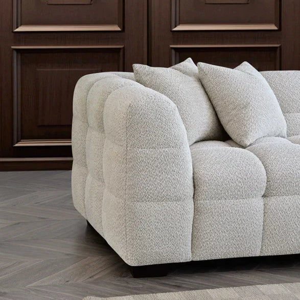 Light grey fabric sofa with tufted upholstery and cushions against wood panel wall