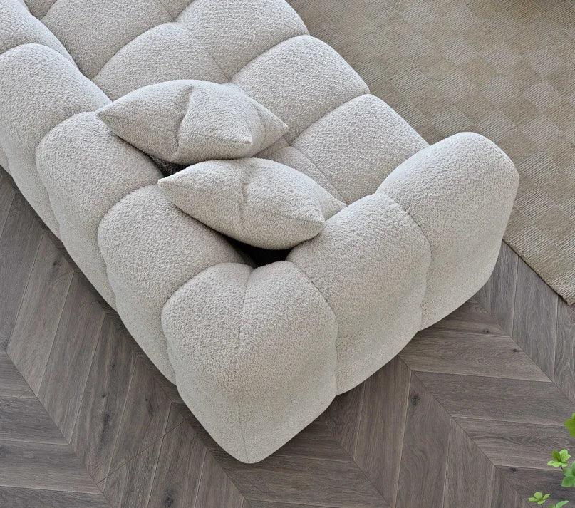 Beige boucle sofa with tufted cushions and two throw pillows on herringbone wood floor