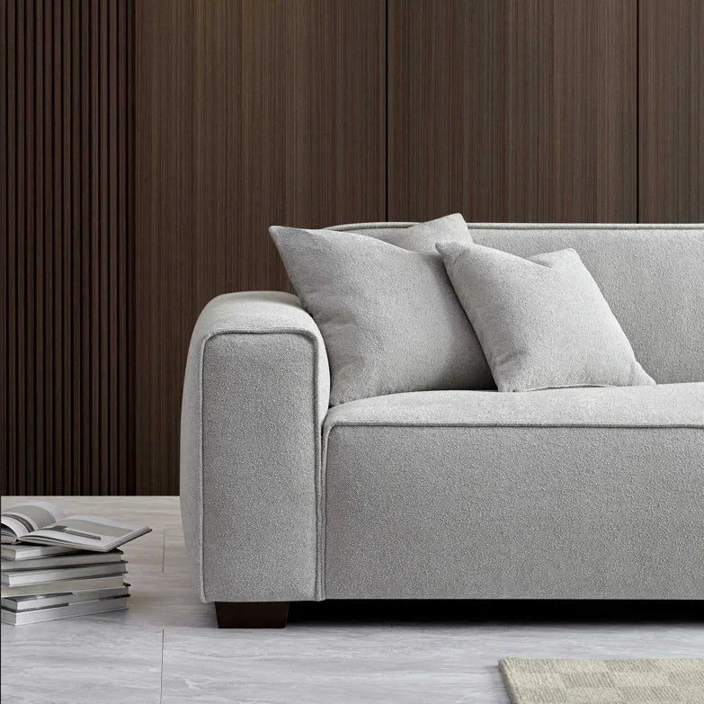 Light grey fabric sofa with two cushions, wooden legs, and books on a modern living room floor