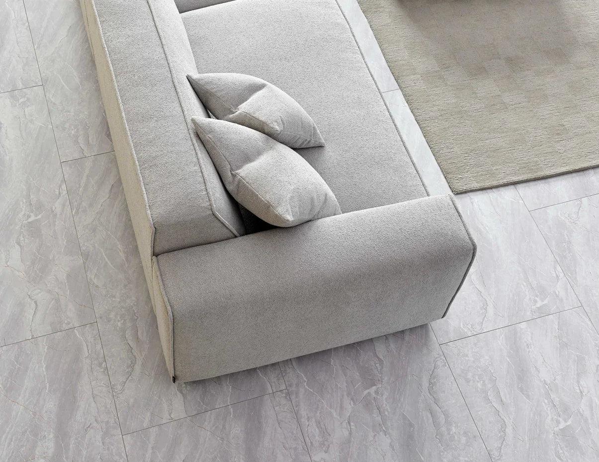 Light grey fabric sofa with two cushions on tiled floor and edge of rug visible