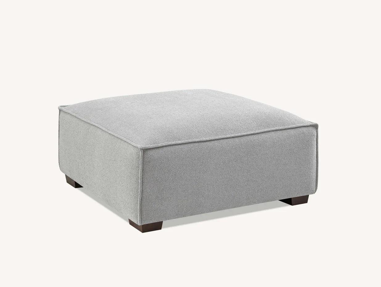 Light grey fabric ottoman with square shape and wooden legs on neutral background
