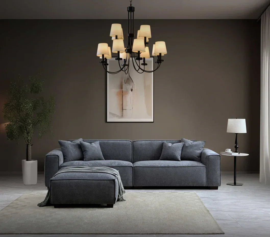 Grey corner sofa with ottoman on neutral rug, accented by table lamp and wall art