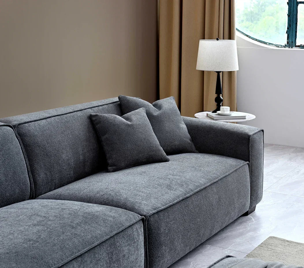 Dark grey fabric sofa with two cushions, beside marble side table and lamp in modern living room