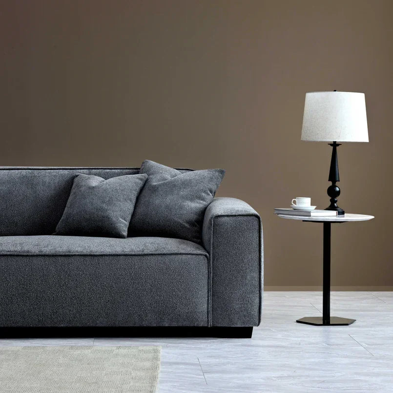 Grey fabric sofa with matching cushions beside a black side table and modern lamp