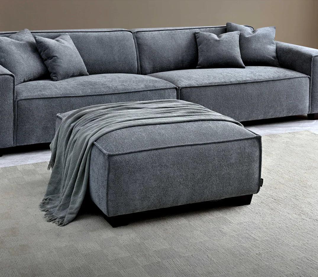 Grey fabric corner sofa with matching ottoman and throw on light textured rug
