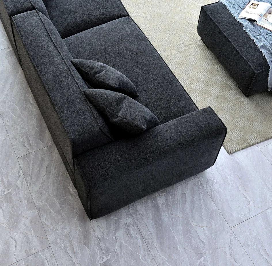 Charcoal fabric sofa with matching cushions on grey tile floor beside ottoman and rug