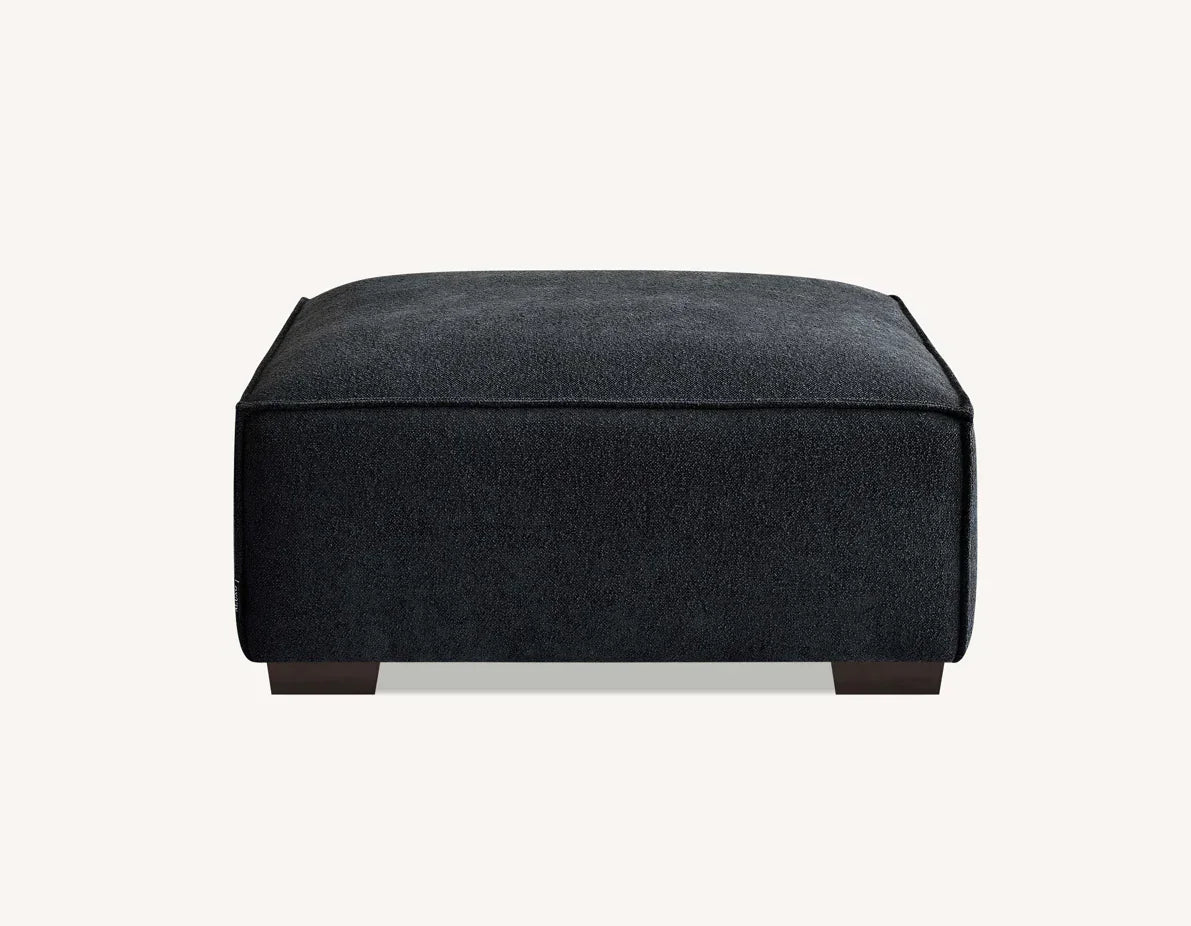 Charcoal fabric ottoman with square design and dark wooden legs on light background