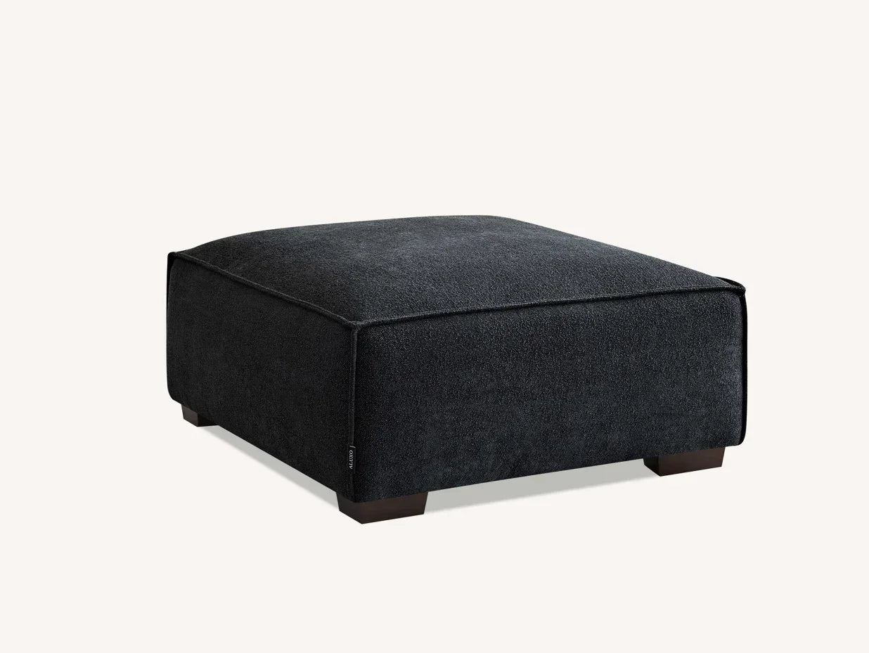 Charcoal fabric ottoman footstool with low wooden legs on neutral background