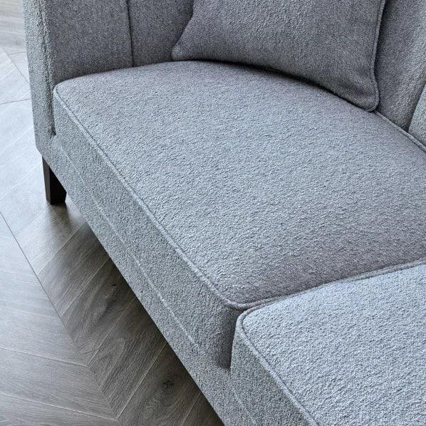 Light grey fabric sofa with cushion and channel tufted backrest on wood floor