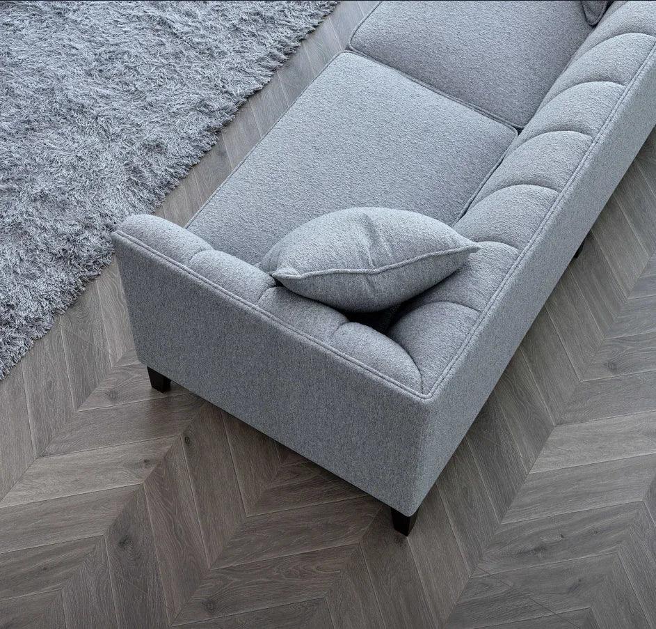 Grey fabric sofa with tufted backrest and cushion on chevron wooden floor next to rug