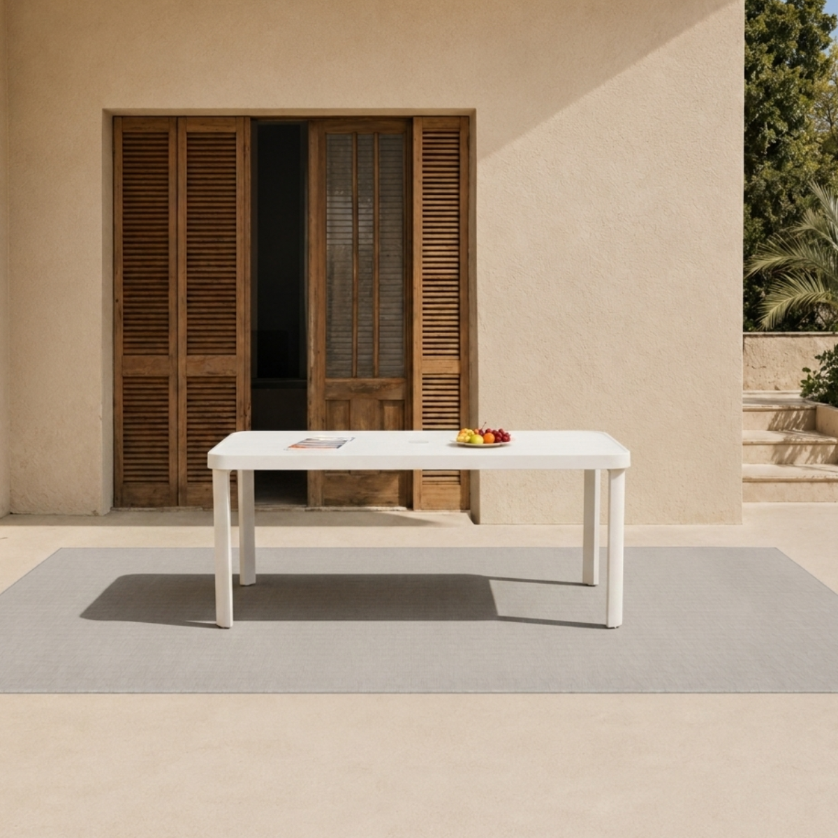 White plastic table on grey textured outdoor mat in front of wooden door panels