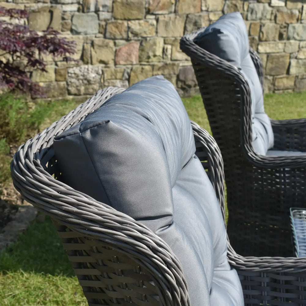 Grey rattan garden chairs with padded cushions next to glass top outdoor table on grass