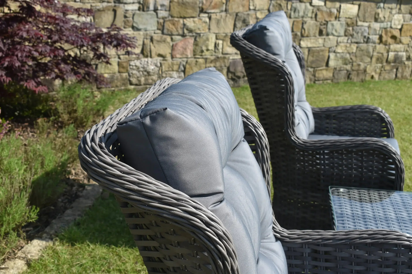 Grey rattan garden chairs with padded cushions next to glass top outdoor table on grass