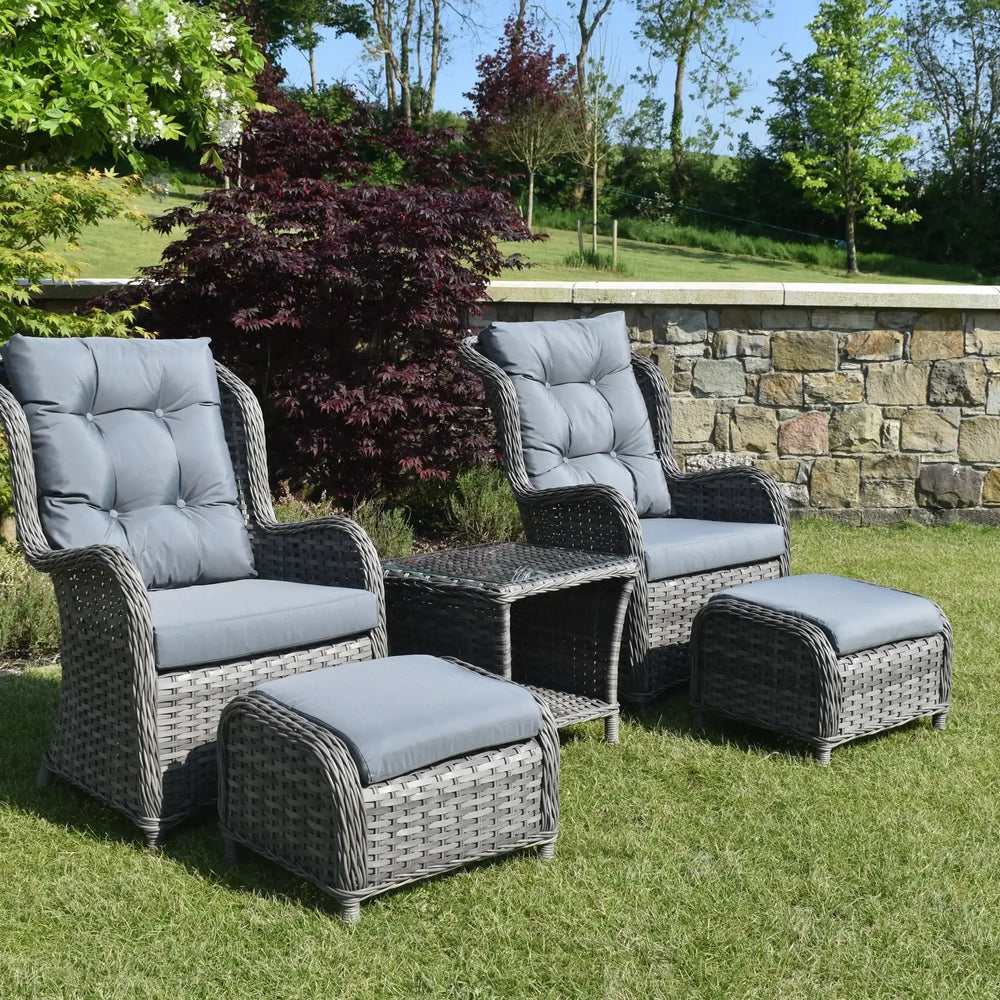 Grey rattan bistro garden set with two armchairs, footstools, and glass top table on lawn