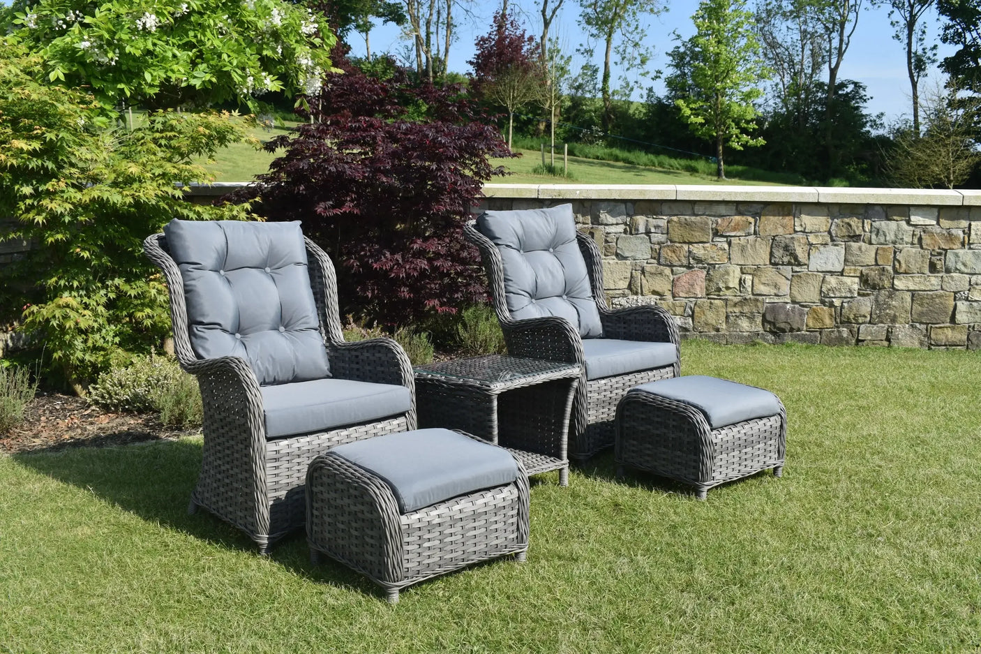 Grey rattan bistro garden set with two armchairs, footstools, and glass top table on lawn