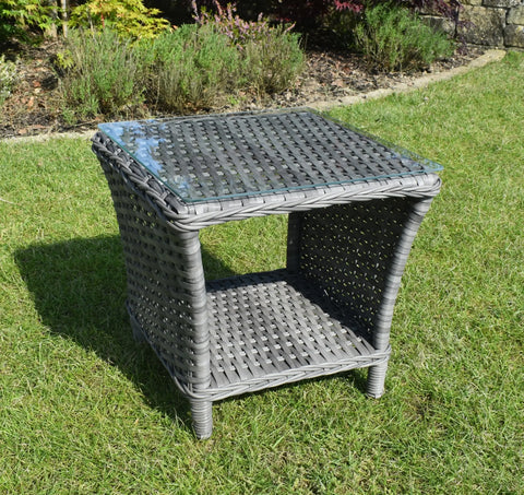 Grey rattan garden side table with glass top and storage shelf on grass