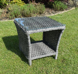 Grey rattan garden side table with glass top and storage shelf on grass