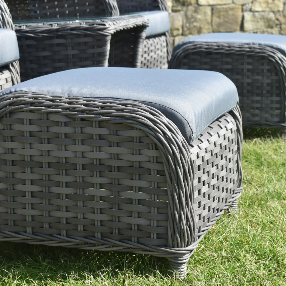 Grey rattan garden seating set with blue cushions on grass, close up of ottomans and armchair