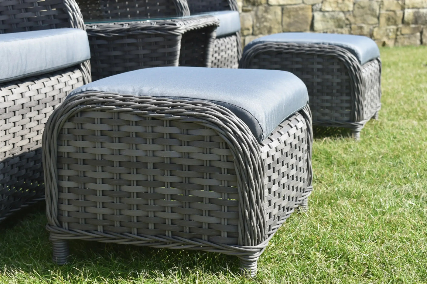 Grey rattan garden seating set with blue cushions on grass, close up of ottomans and armchair