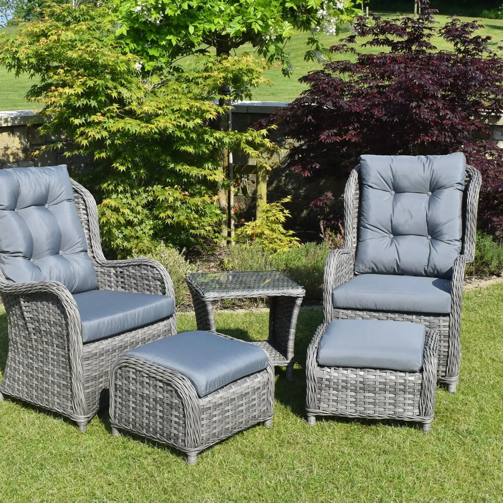 Grey rattan bistro garden set with two armchairs, footstools, and glass top table on lawn