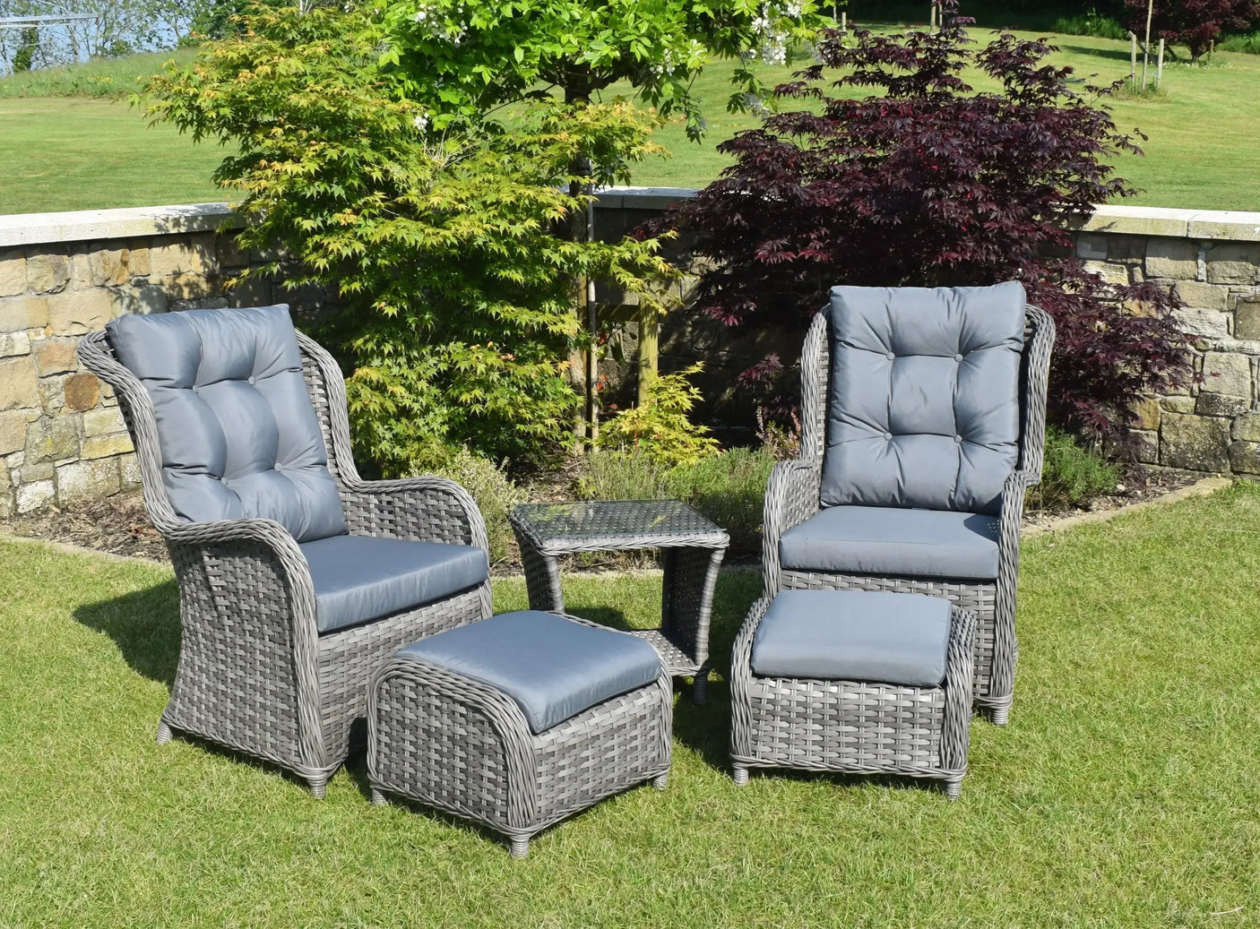 Grey rattan bistro garden set with two armchairs, footstools, and glass top table on lawn