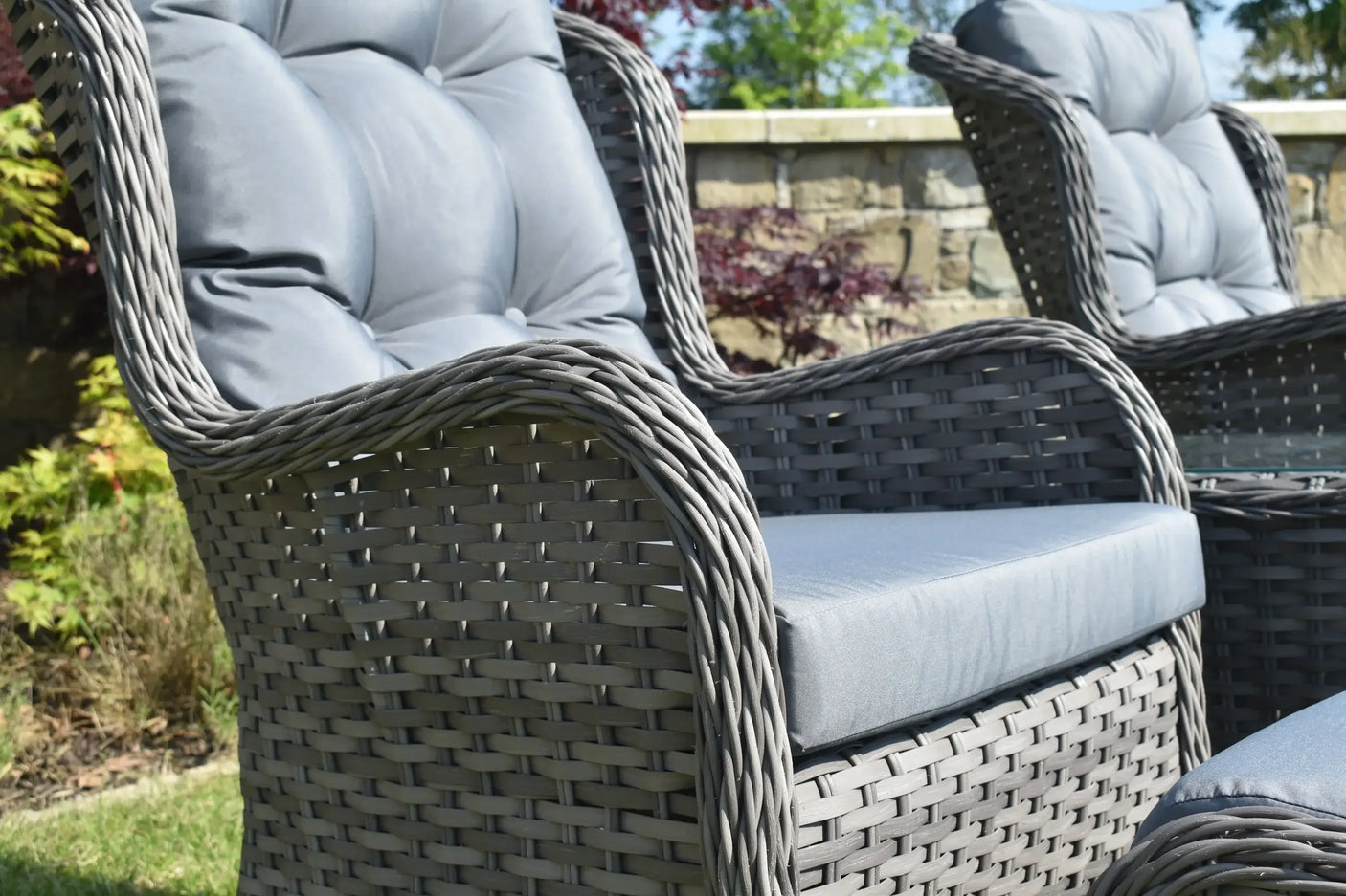 Grey rattan garden chair with padded seat and backrest in outdoor setting
