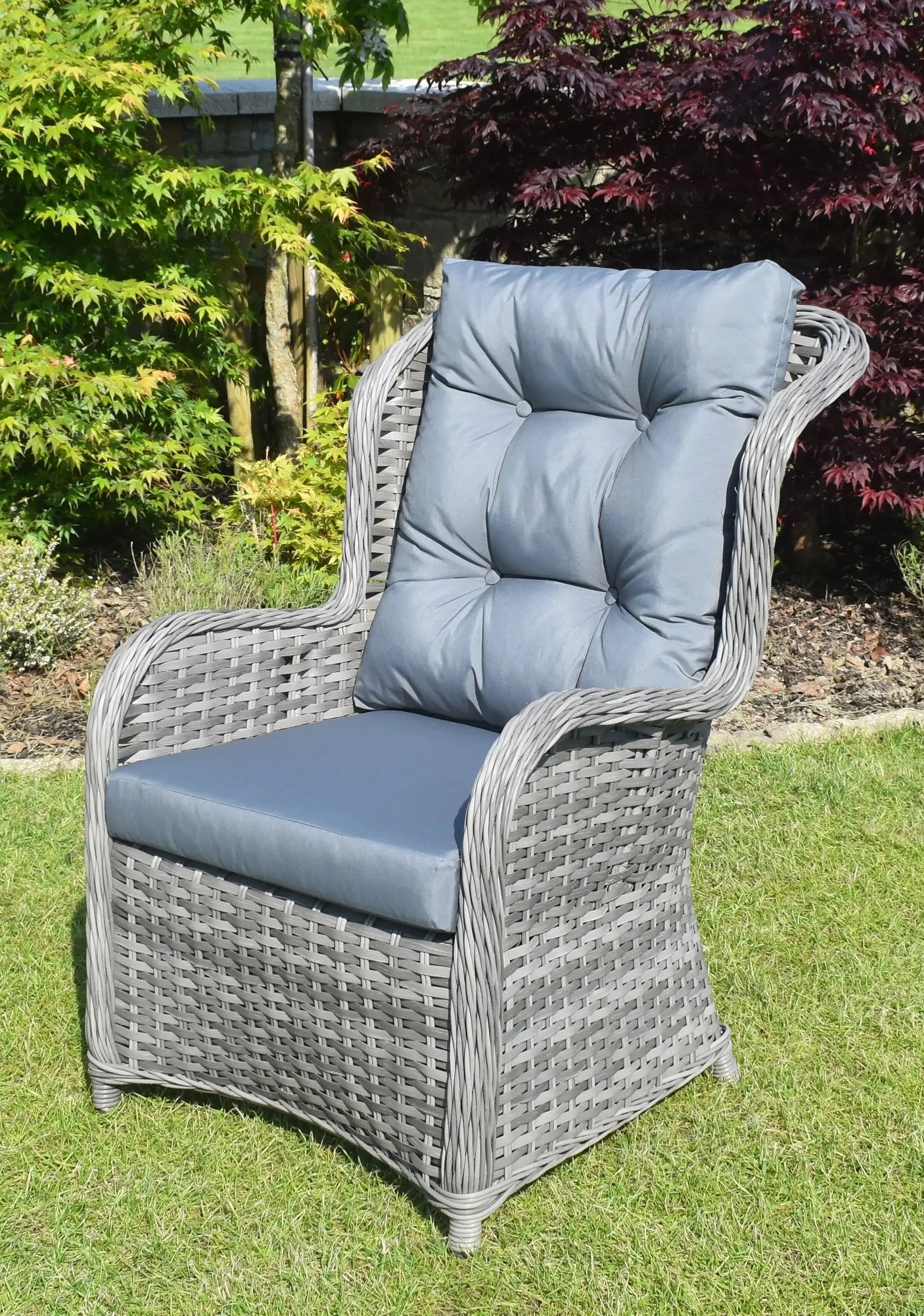 Grey rattan garden armchair with blue padded cushions on lawn