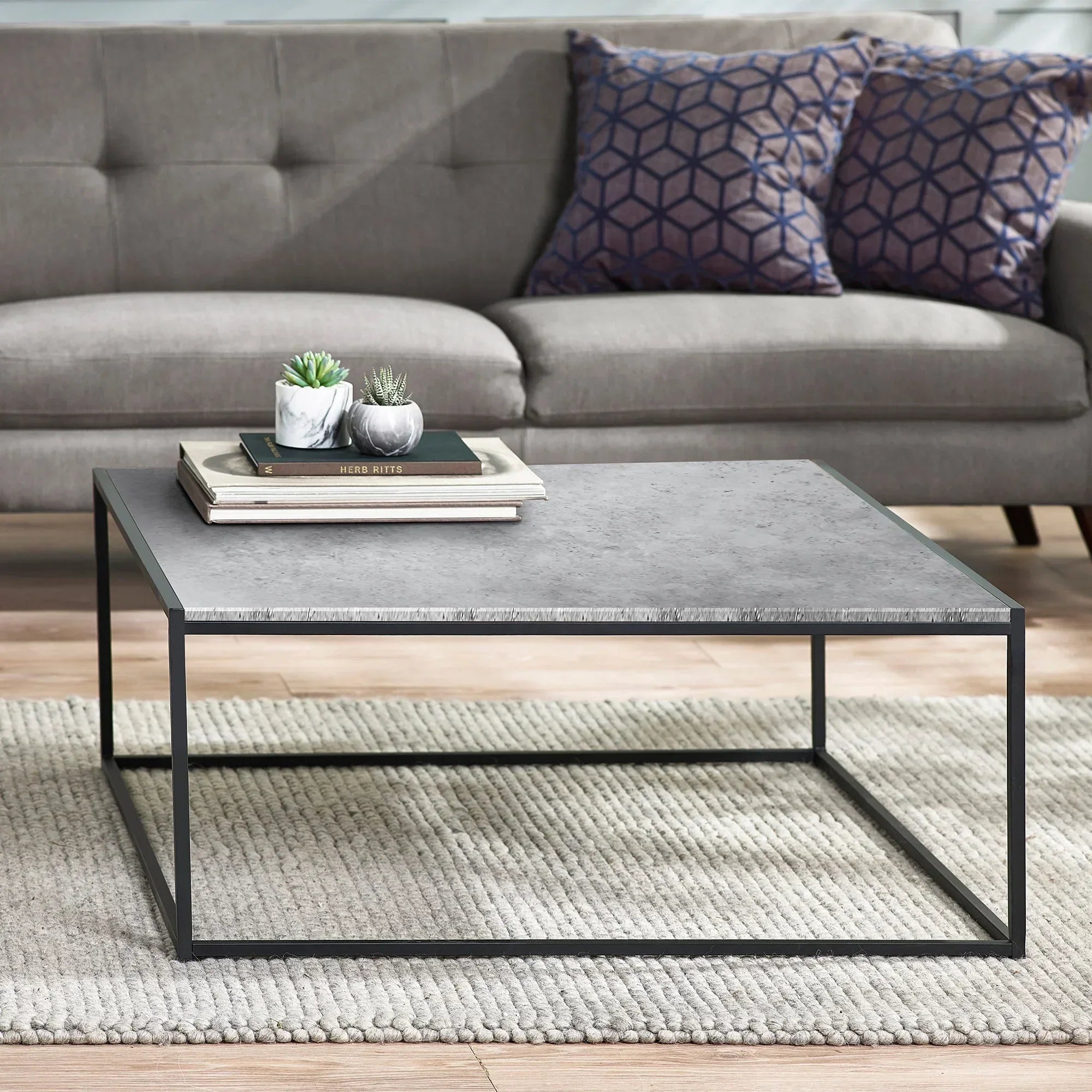Square concrete effect coffee table with metal frame on textured rug in modern living room