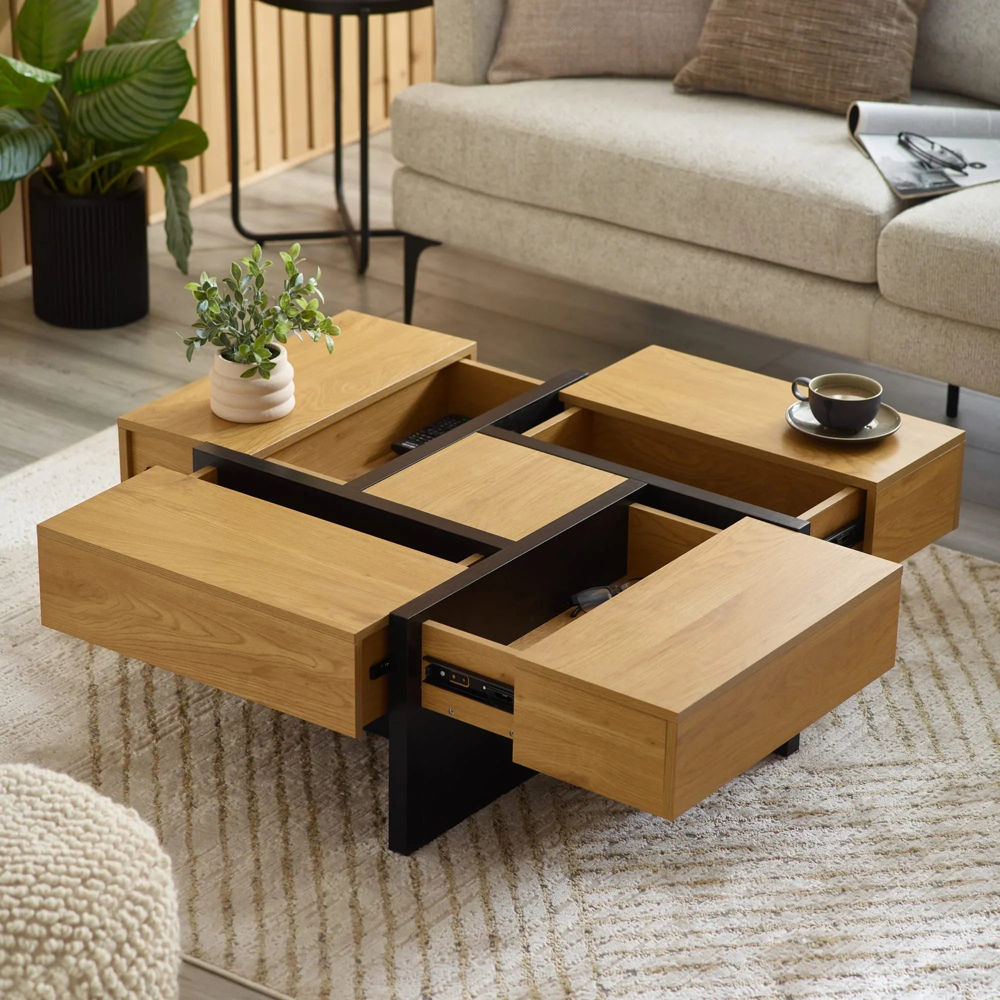 Oak coffee table with black frame, open storage drawers, cup and plant in modern living room