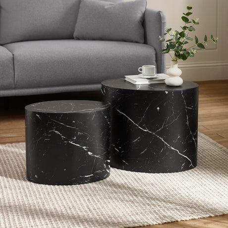 Black marble effect oval nest tables with decorative vases and books, beside a grey curved sofa on wood floor.