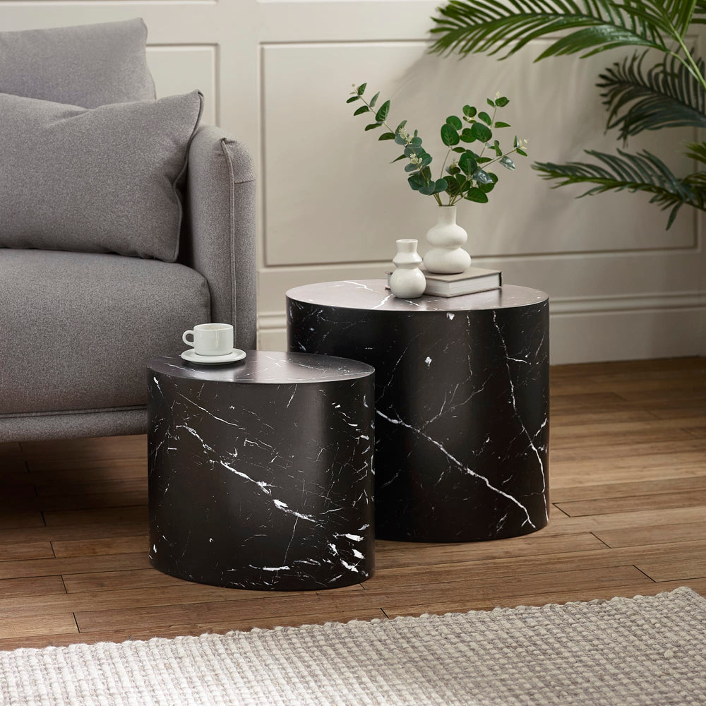 Black marble effect oval nest tables with cups on them, next to a grey sofa and a cream rug on wood floor.