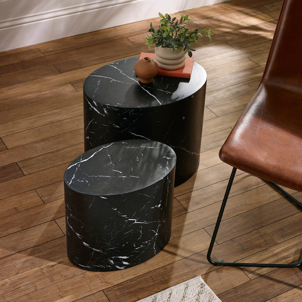 Two black oval nest tables with white marble veins on wooden floor next to brown leather chair