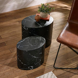 Two black oval nest tables with white marble veins on wooden floor next to brown leather chair