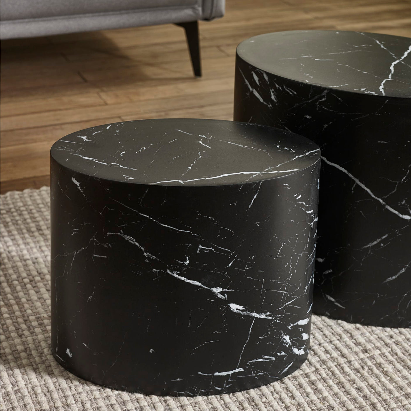 Small and large black oval tables with white marble veins on beige rug in living room setting