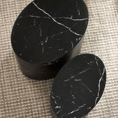 Close-up of black oval nest tables showing white marble veining and textured beige rug underneath