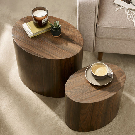 Overhead view of two dark wood oval nest tables with candle and cup, beside beige sofa on carpet