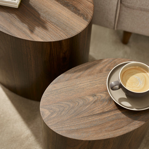 Close-up of dark wood oval table tops with visible grain and coffee cup on smaller table beside sofa