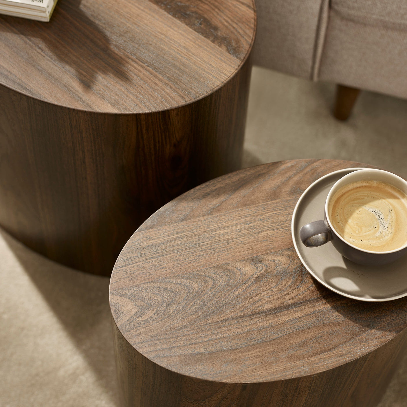 Close-up of dark wood oval table tops with visible grain and coffee cup on smaller table beside sofa