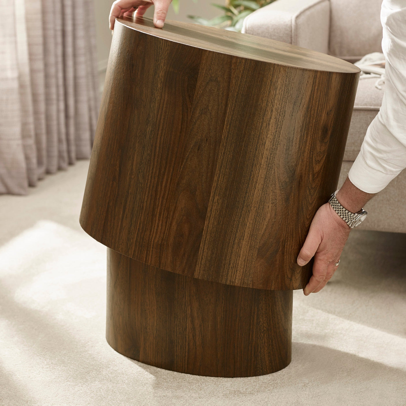 Hands lifting smaller dark wood oval table from beside larger table on light carpet near sofa