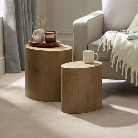 Two light oak oval nest tables beside white fabric sofa, one with coffee cup, in soft carpeted room